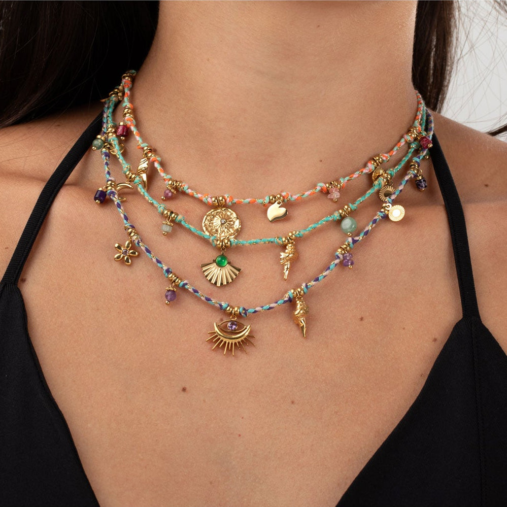 collar boho chic de cordón o hilo trenzado morado, azul y dorado. tiene abalorios dorados como el ojo turco y la caracola. Piedra natural amatista. Es de acero hipoalergénico