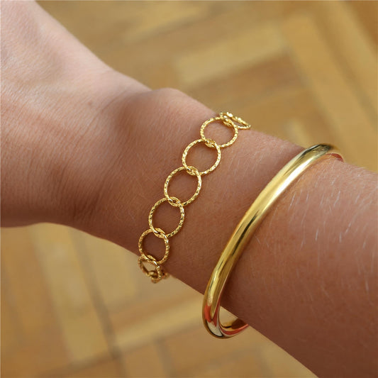 Pulsera Olimpo dorada puesta en la muñeca: cadena de aros redondos tallados, acero hipoalergénico resistente al agua