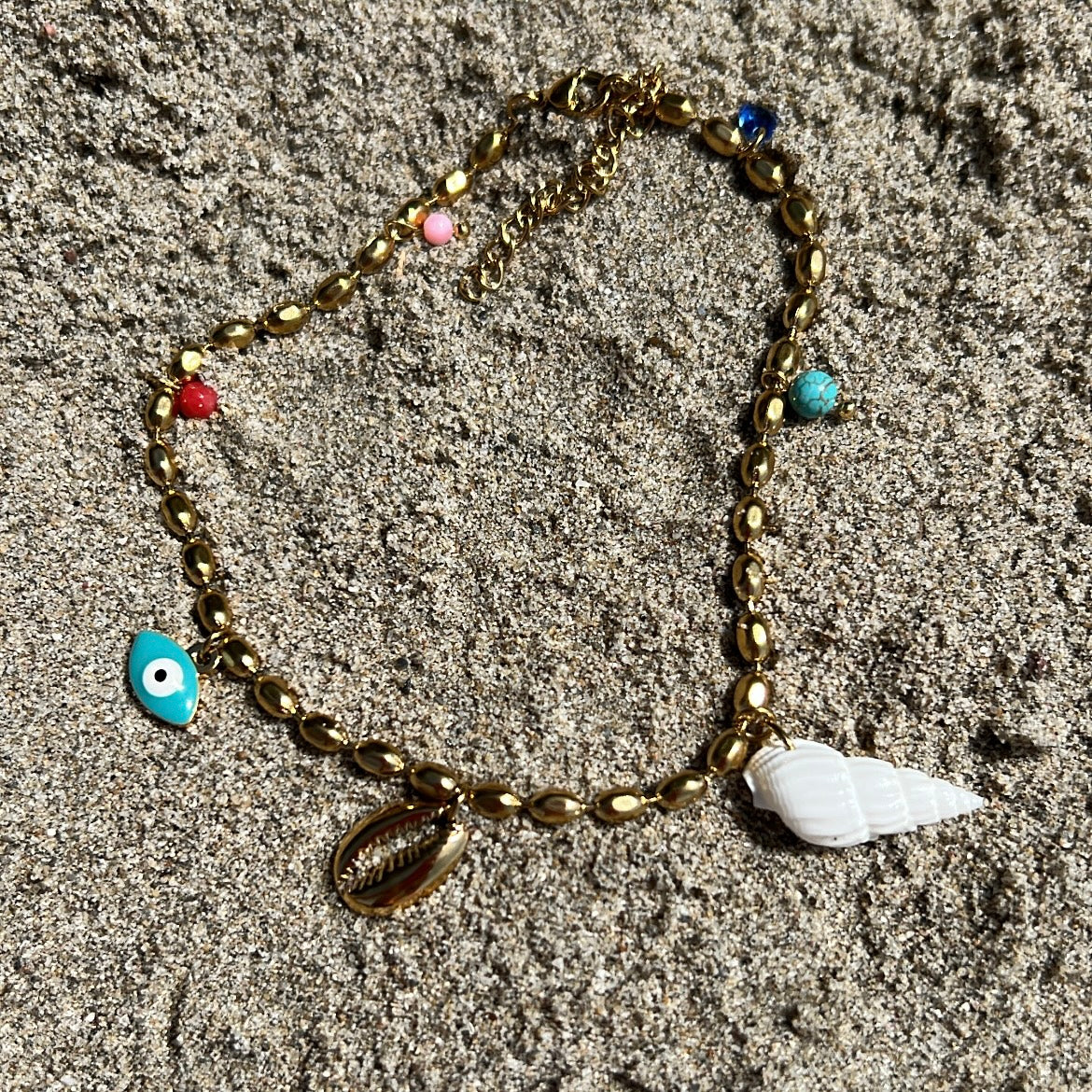 tobillera griega para verano resistente al agua en colores dorado,  azul turquesa y coral. tiene abalorios de concha y ojo turco. Es de acero hipoalergénico