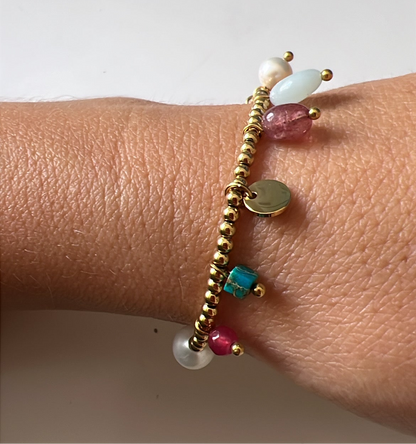 pulsera elástica waterproof o resistente al agua confeccionada en acero con baño de oro 18 kilates. Tiene abalorios de colores imitando piedra natural y perla cultivada. 