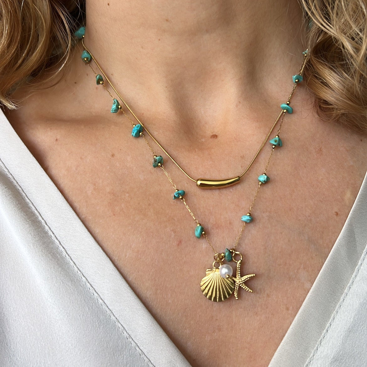 COLLAR waterproof o resistente al agua confeccionada en acero con baño de oro 18 kilates. Tiene abalorios de colores imitando piedra natural turqyesa y perla cultivada. también tiene colgantes de estrella de mar y concha. 