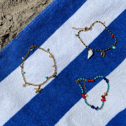 tobillera griega para verano resistente al agua en colores dorado,  azul turquesa y coral. tiene abalorios de concha y ojo turco. Es de acero hipoalergénico