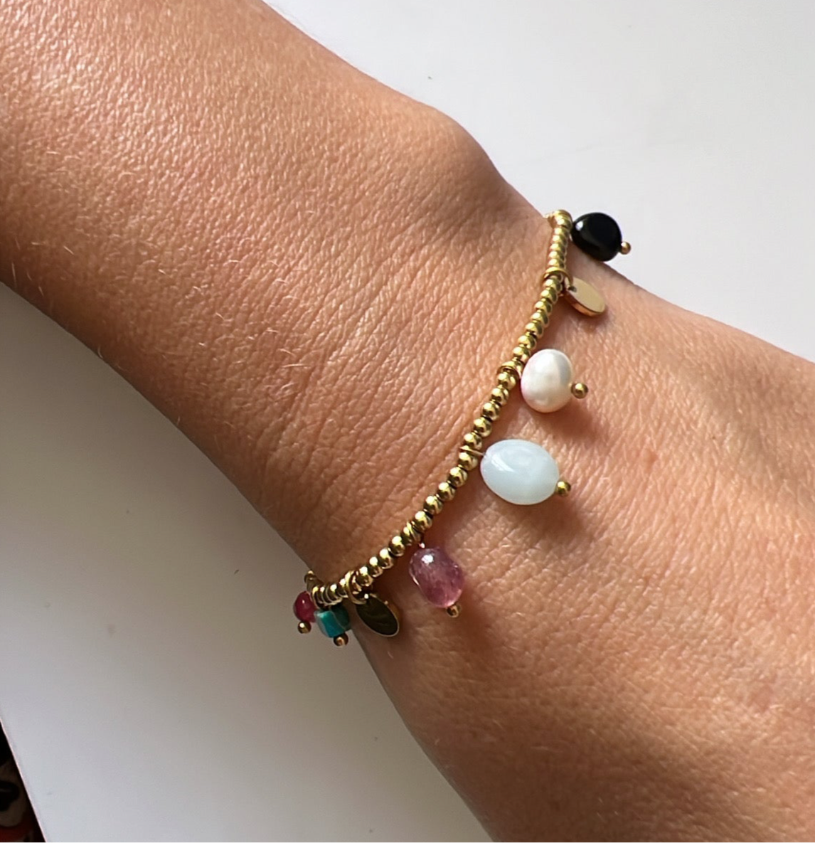 pulsera elástica waterproof o resistente al agua confeccionada en acero con baño de oro 18 kilates. Tiene abalorios de colores imitando piedra natural y perla cultivada. 