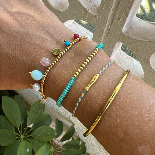 pulsera elástica waterproof o resistente al agua confeccionada en acero con baño de oro 18 kilates. Tiene abalorios de colores imitando piedra natural y perla cultivada. 