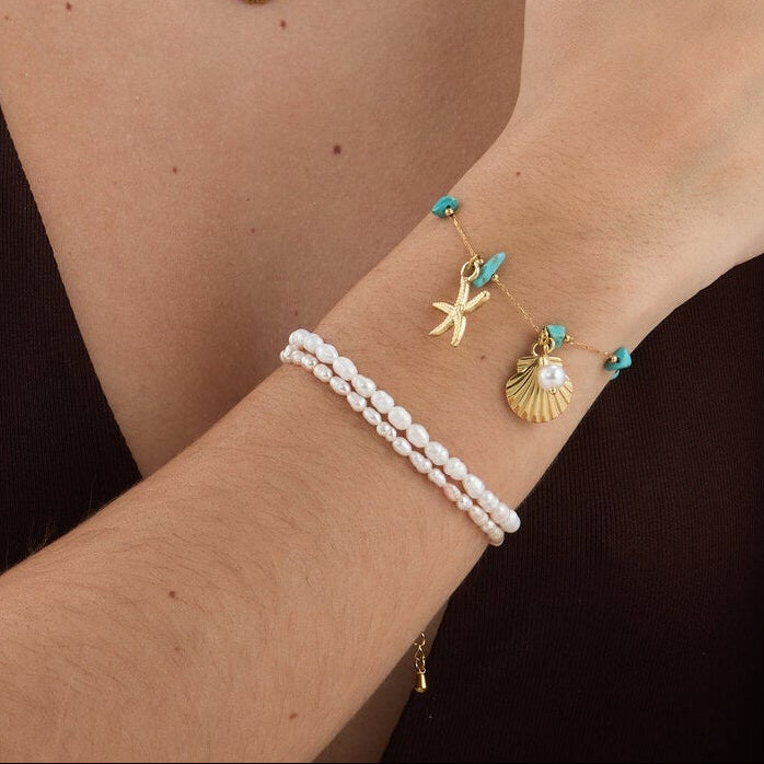 pulsera waterproof o resistente al agua confeccionada en acero con baño de oro 18 kilates. Tiene abalorios de colores imitando piedra natural turqyesa y perla cultivada. también tiene colgantes de estrella de mar y concha. 

