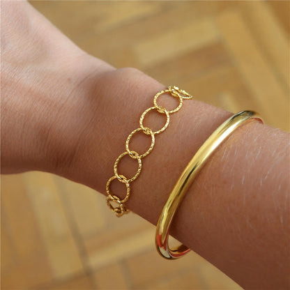 Pulsera Olimpo dorada puesta en la muñeca: cadena de aros redondos tallados, acero hipoalergénico resistente al agua