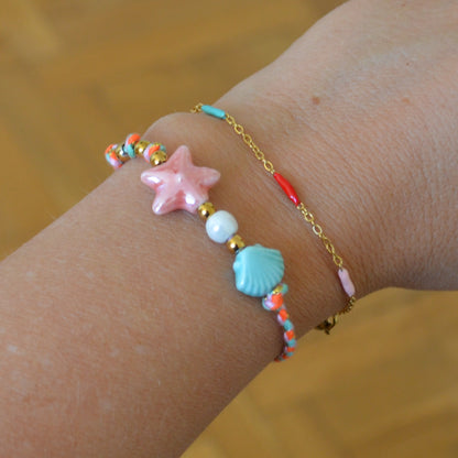 pulsera DE VERANO waterproof o resistente al agua confeccionada con cordón rosa con abalorios de cerámica y acero dorado.  Cierre ajustable, colgante de estrella de mar y concha en color rosa y azul turquesa. Ideal para regalar a mujeres, niñas y adolescentes en vacaciones.