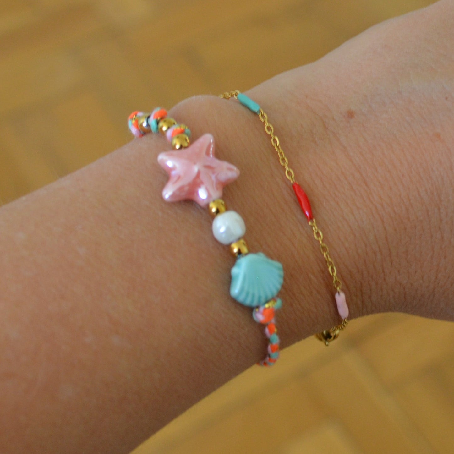 pulsera DE VERANO waterproof o resistente al agua confeccionada con cordón rosa con abalorios de cerámica y acero dorado.  Cierre ajustable, colgante de estrella de mar y concha en color rosa y azul turquesa. Ideal para regalar a mujeres, niñas y adolescentes en vacaciones.