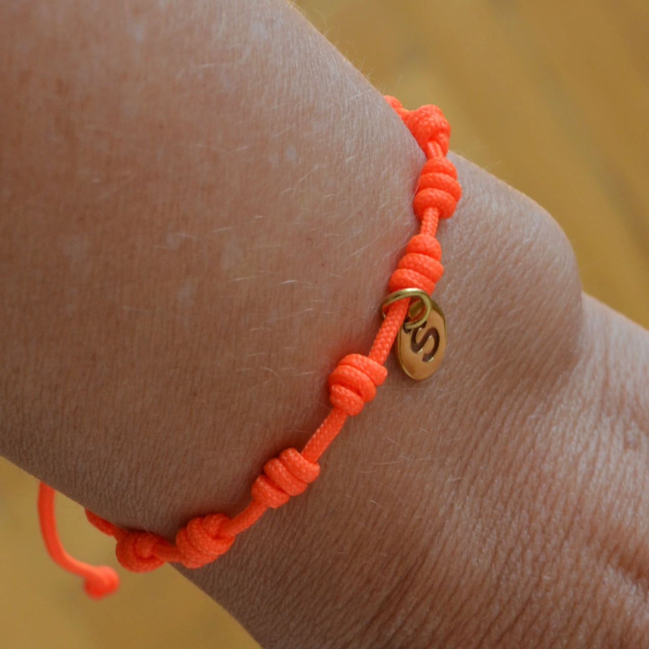Pulsera para verano naranja fluor con nudos de colores. Está confeccionada en cordón encerado con nudos. Se puede personalizar con un colgante de letra con las iniciales de los hijos o los nietos. El cierre es ajustable. Es un regalo perfecto para niñas o para el dia de la madre. 