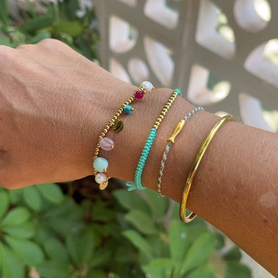 pulsera elástica waterproof o resistente al agua confeccionada en acero con baño de oro 18 kilates. Tiene abalorios de colores imitando piedra natural y perla cultivada. 