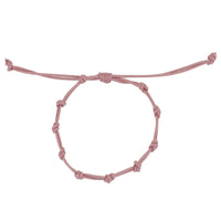 Pulsera para verano con nudos de color rosa claro . Está confeccionada en cordón encerado con dos nudos. Se puede personalizar con un colgante de letra o charms de estrella, concha o luna. El cierre es ajustable.