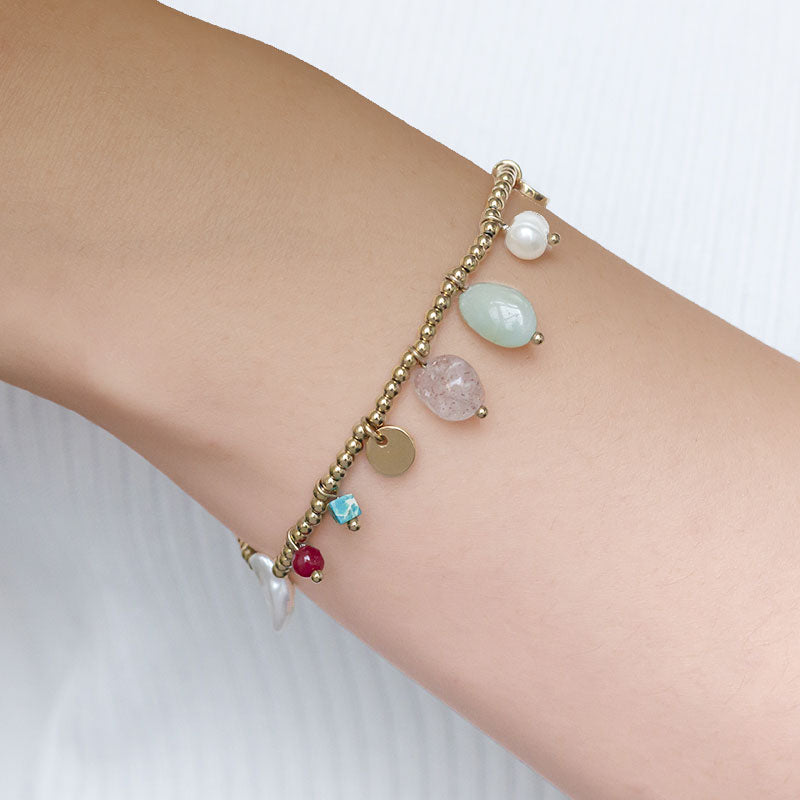 pulsera elástica waterproof o resistente al agua confeccionada en acero con baño de oro 18 kilates. Tiene abalorios de colores imitando piedra natural y perla cultivada. 